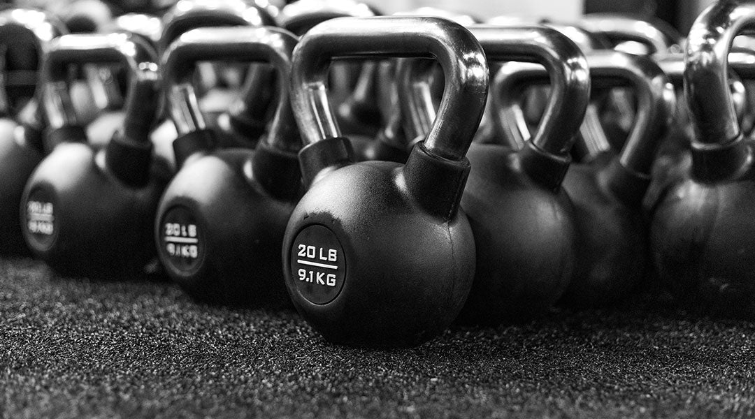 A black and white image of a large number of kettlebells lined up in rows and columns on a carpet.
