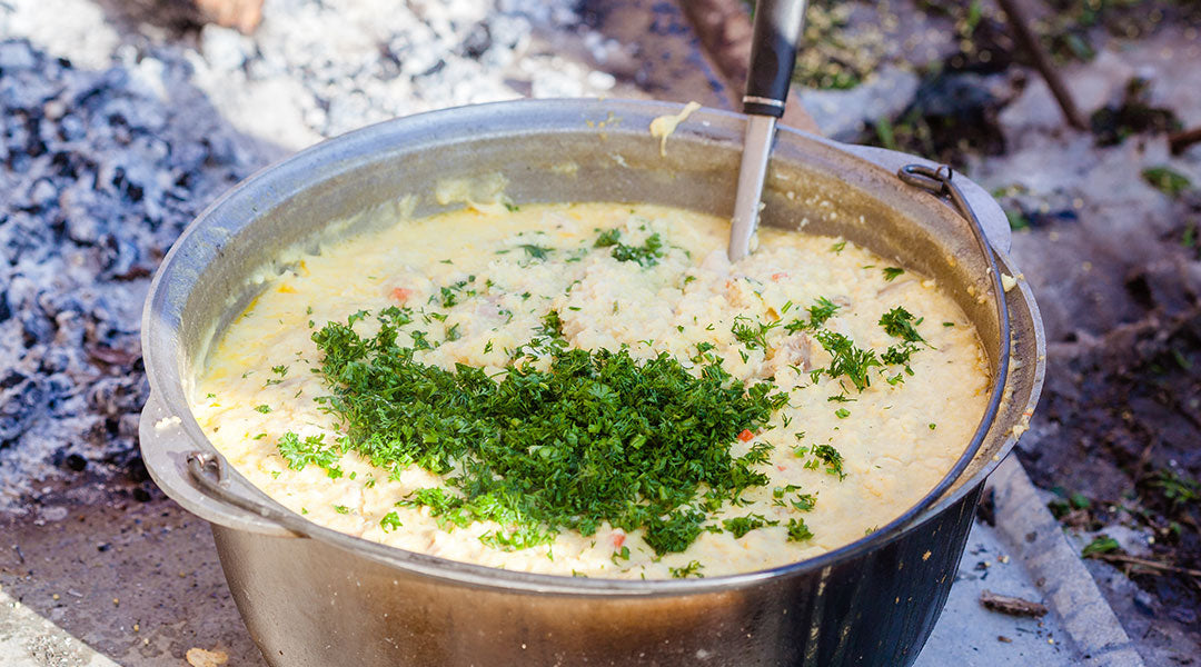 A metal bowl full of broccoli cheddar soup with green garnish on top.