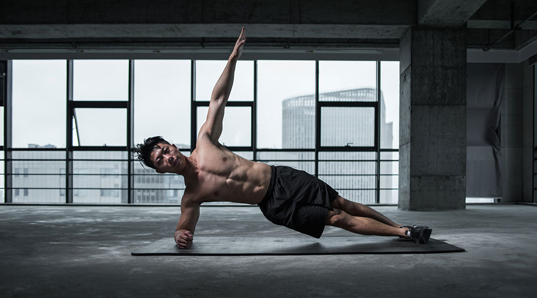 Shirtless man in side plank position with one arm raised