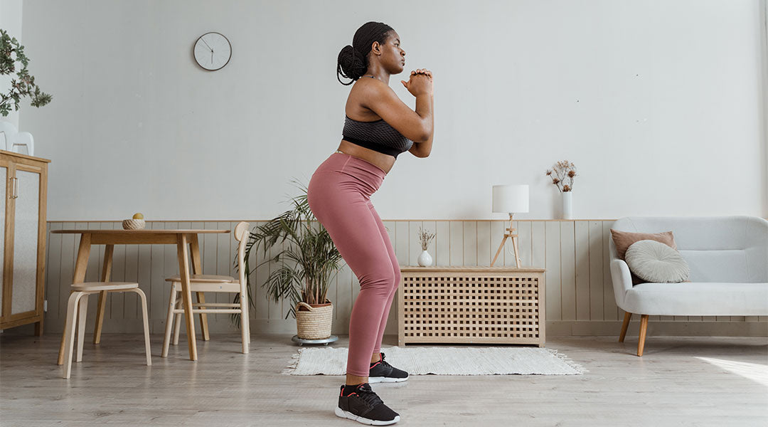 Woman in living room wearing athletic clothing in a starting squat position.