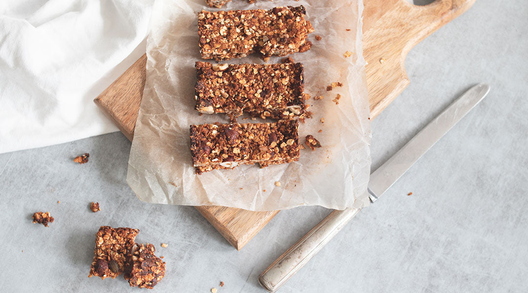 Crumbly oatmeal protein bars on a piece of parchment paper on a small wooden cutting board against a grey marble background with a table knife and a broken piece of protein bar off to the side.