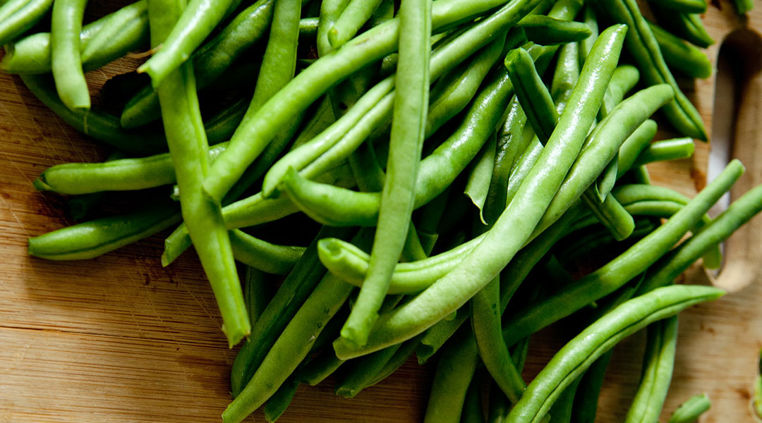 A pile of nice, fresh looking green beans already topped on a wooden cutting board.