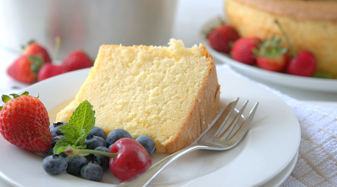A slice of yellowish white cake laying on its side on a white plate with a silver fork and a small pile of berries.